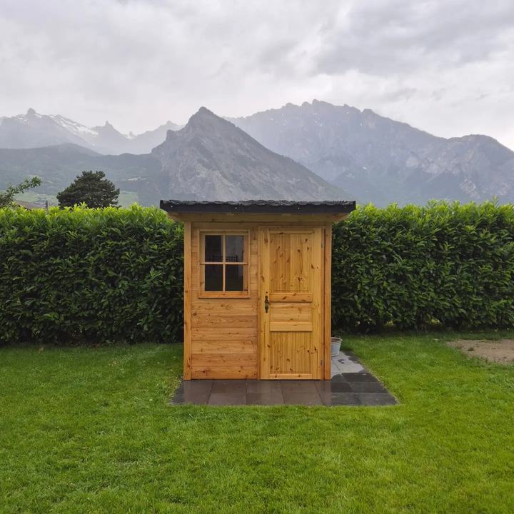 Petite cabane de jardin en mélèze dans un jardin, montagnes en arrière-plan